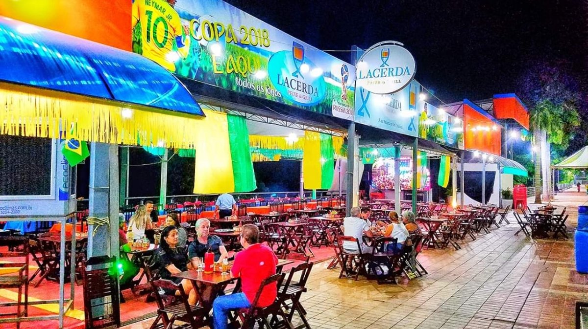 Área externa do Lacerda cheia de gente à noite, com mesas ocupadas e clima festivo