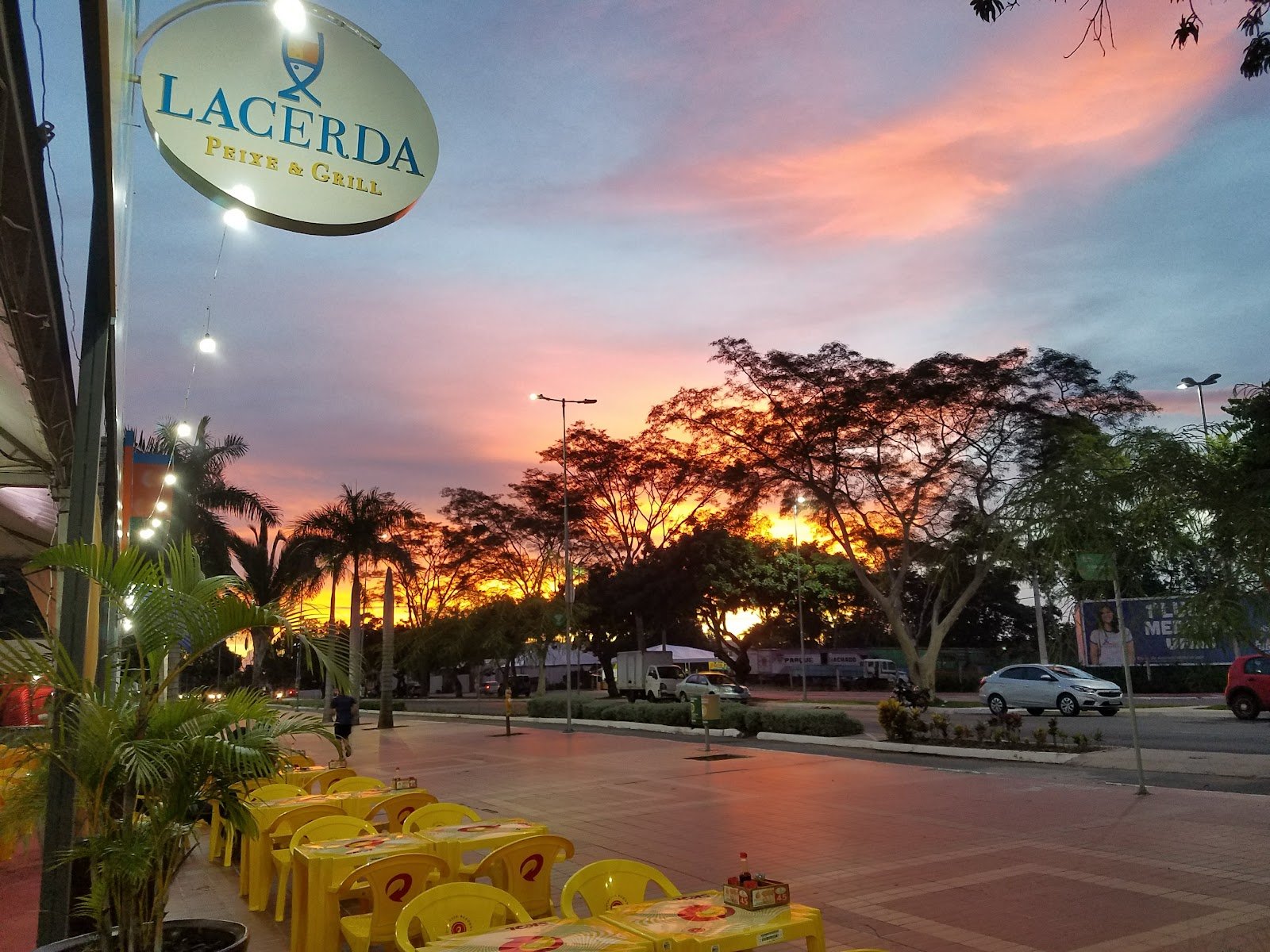 Pôr do sol na orla do Porto com a placa do Lacerda Peixe e Grill e as mesas à beira do Rio Cuiabá